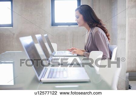 Stock Image - Young woman and row of laptops in boardroom. Fotosearch