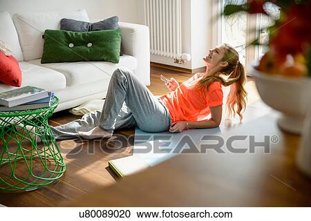 Stock Image - Young woman holding smartphone whilst lounging on floor. Fotosearch