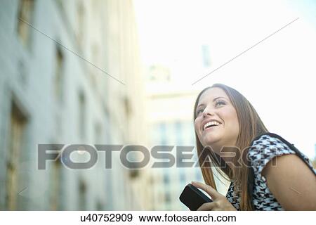 Stock Photo - Young woman in city with mobile phone. Fotosearch