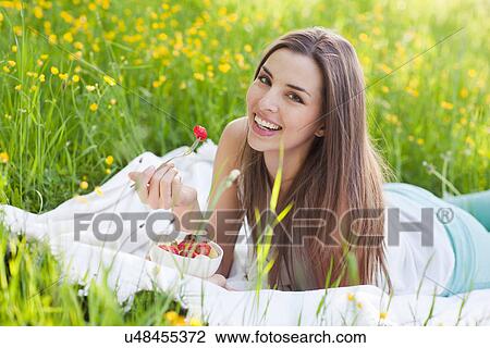 Stock Image - Young woman in field of buttercups eating strawberries. Fotosearch