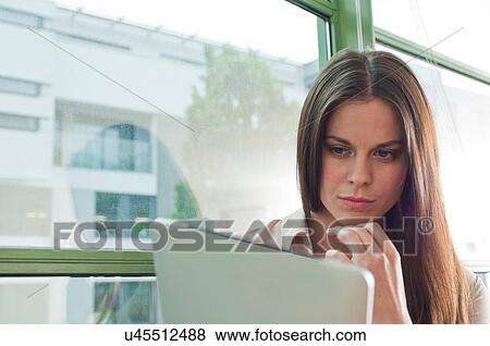 Stock Photo - Young woman in office looking at digital tablet. Fotosearch