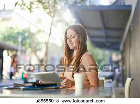 Stock Photo - Young woman looking at digital tablet in street cafe. Fotosearch