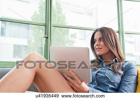 Young woman lounging on sofa holding digital tablet View Large Photo Image Stock Photo - Young woman lounging on sofa holding digital tablet. Fotosearch