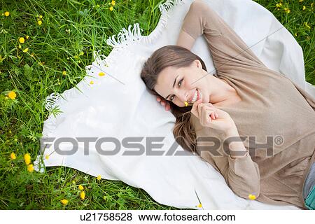 Young woman lying on picnic blanket holding buttercup View Large Photo Image Stock Photo - Young woman lying on picnic blanket holding buttercup. Fotosearch