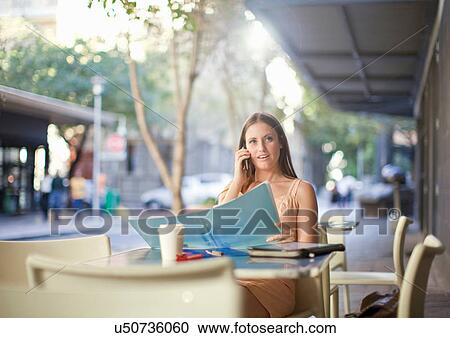 Stock Image - Young woman on mobile in street cafe. Fotosearch