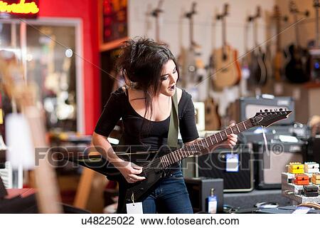 Stock Image - Young woman playing electric guitar in music store. Fotosearch