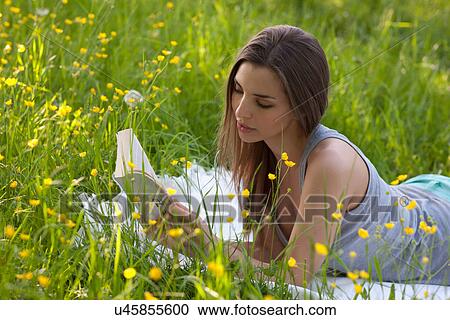 Stock Image - Young woman reading in field of buttercups. Fotosearch