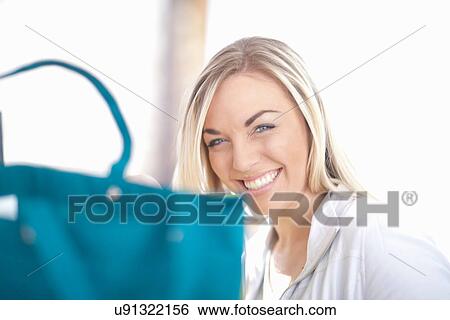 Stock Photograph - Young woman sitting behind turquoise shopping bag. Fotosearch