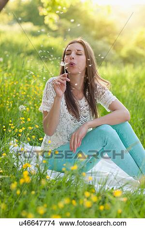 Young woman sitting in meadow blowing dandelion clock View Large Photo Image Picture - Young woman sitting in meadow blowing dandelion clock. Fotosearch