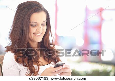 Stock Image - Young woman sitting outdoors texting on mobile. Fotosearch