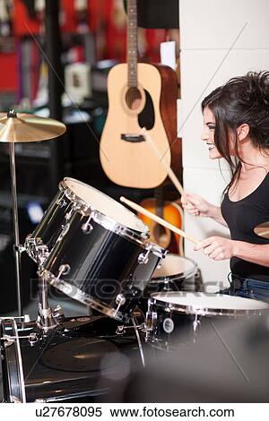 Stock Photography - Young woman trying drum kit in music store. Fotosearch