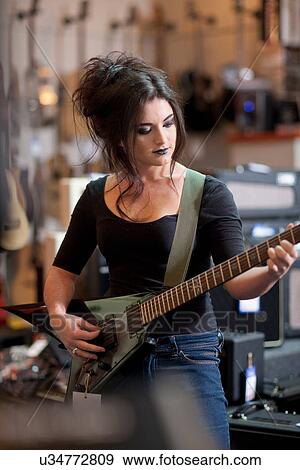 Stock Photo - Young woman trying electric guitar in music store. Fotosearch