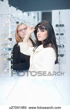 Stock Photography - Young woman trying on sunglasses in opticians shop. Fotosearch