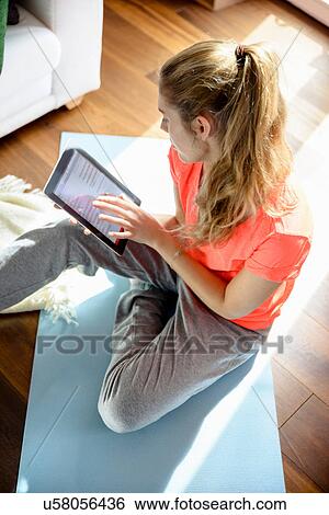 Young woman using digital tablet whilst sitting on floor View Large Photo Image Stock Photograph - Young woman using digital tablet whilst sitting on floor. Fotosearch