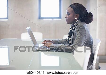 Stock Image - Young woman using laptop in boardroom. Fotosearch