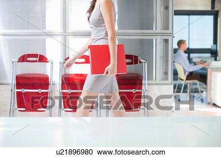 Stock Image - Young woman walking through office. Fotosearch