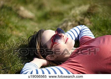 Stock Photography - Young woman wearing heart shape sunglasses lying on grass. Fotosearch