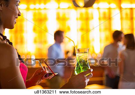 Stock Image - Young woman with cocktail and sunglasses in club. Fotosearch