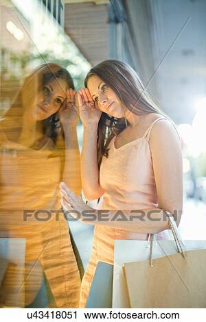 Stock Image - Young woman with shopping bags looking in shop window. Fotosearch