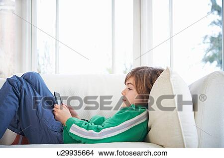 Picture - Boy on sofa using digital tablet. Fotosearch