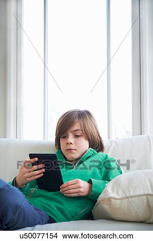 Boy on sofa using digital tablet View Large Photo Image Picture - Boy on sofa using digital tablet. Fotosearch