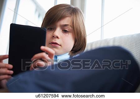 Boy on sofa using digital tablet View Large Photo Image Picture - Boy on sofa using digital tablet. Fotosearch