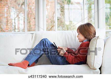 Boy on sofa using digital tablet View Large Photo Image Stock Image - Boy on sofa using digital tablet. Fotosearch