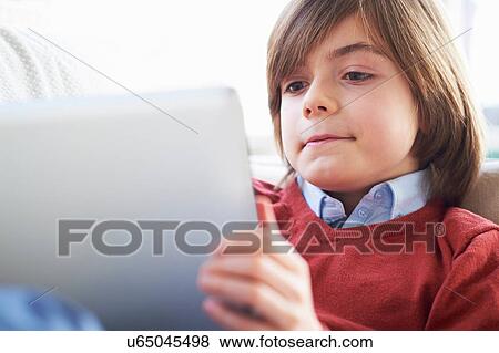 Boy on sofa using digital tablet View Large Photo Image Stock Photo - Boy on sofa using digital tablet. Fotosearch