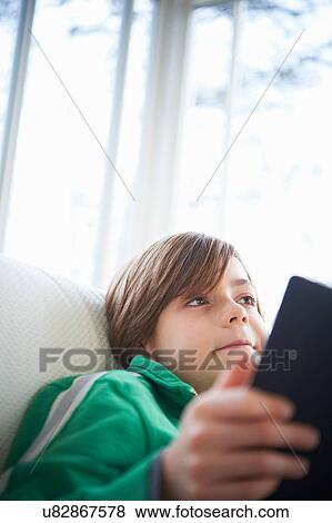 Stock Photo - Boy on sofa using digital tablet. Fotosearch