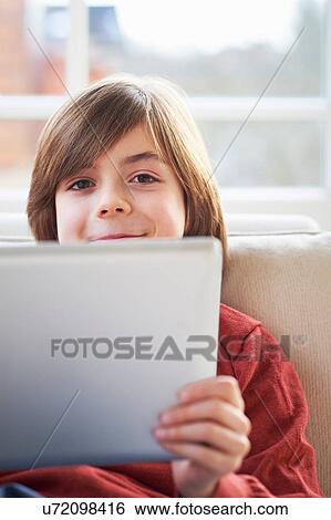 Stock Photograph - Boy on sofa using digital tablet. Fotosearch