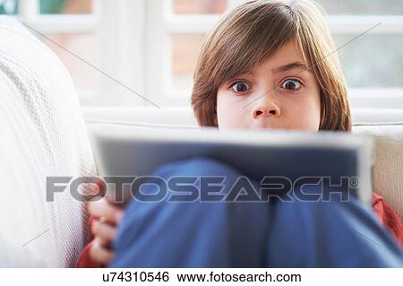 Stock Photograph - Boy on sofa using digital tablet. Fotosearch