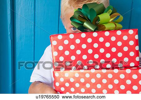 Stock Image - Boy peeping behind gifts in hand. Fotosearch
