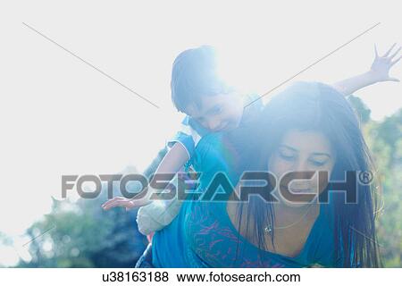 Stock Photo - Boy riding on mother's back with arms stretched out. Fotosearch