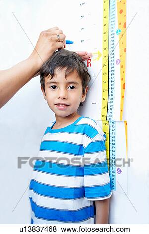 Stock Photo - Boy standing against height chart being measured. Fotosearch