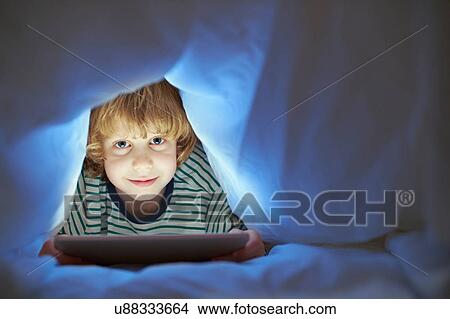 Boy underneath duvet using digital tablet View Large Photo Image Picture - Boy underneath duvet using digital tablet. Fotosearch