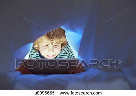 Stock Image - Boy underneath duvet using digital tablet. Fotosearch