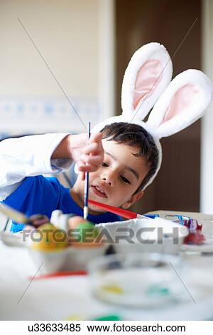 Boy wearing bunny ears painting Easter eggs View Large Photo Image Stock Photography - Boy wearing bunny ears painting Easter eggs. Fotosearch