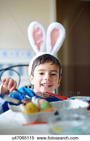 Stock Photography - Boy wearing bunny ears painting Easter eggs. Fotosearch