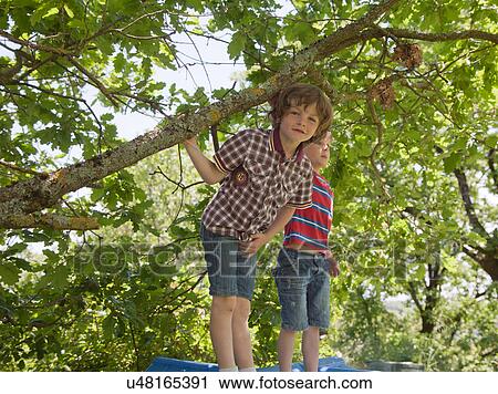 Stock Image - Boys sitting on roof of tree house. Fotosearch
