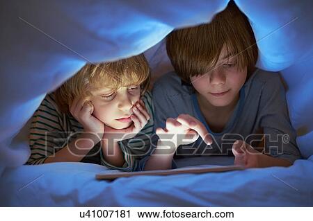 Stock Image - Brothers underneath duvet using digital tablet. Fotosearch