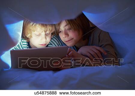 Stock Photo - Brothers underneath duvet using digital tablet. Fotosearch