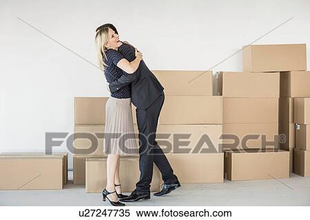 Stock Photography - Businessman and -woman hugging in front of stack of cardboard boxes. Fotosearch