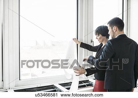 Stock Image - Businesspeople looking at blueprint. Fotosearch