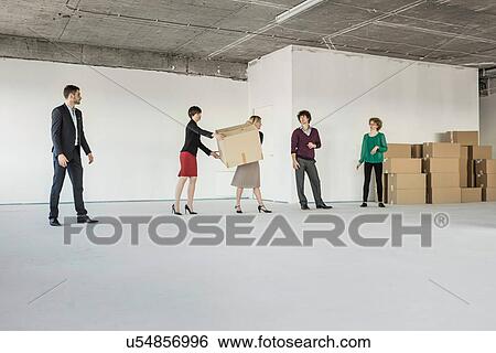 Businesspeople moving cardboard boxes around unfinished office interior View Large Photo Image Stock Photograph - Businesspeople moving cardboard boxes around unfinished office interior. Fotosearch