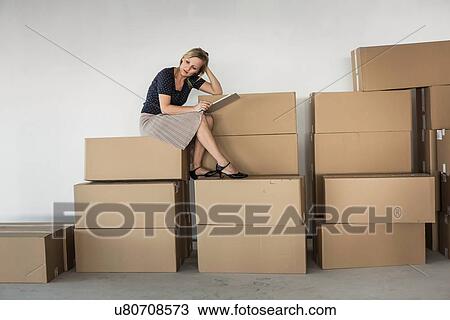 Stock Image - Businesswoman sitting on stack of cardboard boxes. Fotosearch