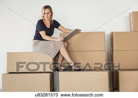 Stock Image - Businesswoman sitting on stack of cardboard boxes. Fotosearch