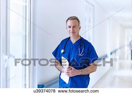 Doctor standing in corridor holding medical records View Large Photo Image Stock Photo - Doctor standing in corridor holding medical records. Fotosearch