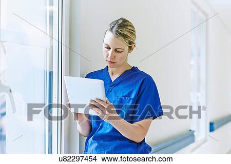 Picture - Doctor standing in corridor looking at digital tablet. Fotosearch