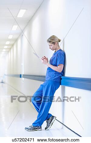 Stock Image - Doctor standing in corridor looking at digital tablet. Fotosearch