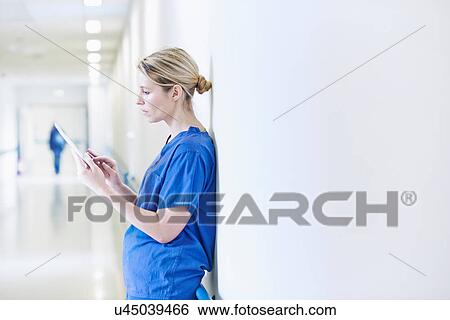 Stock Photograph - Doctor standing in corridor looking at digital tablet. Fotosearch